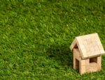 A small, model wooden house on a patch of green grass